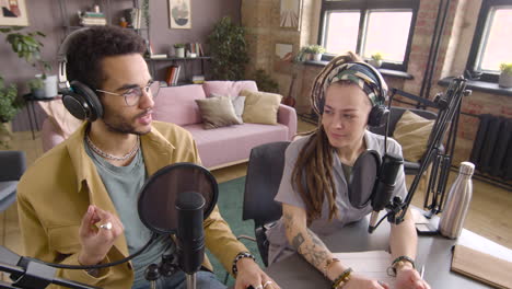 high angle view of young african american man and caucasian woman wearing headphones sitting at a table with microphones while they recording a podcast