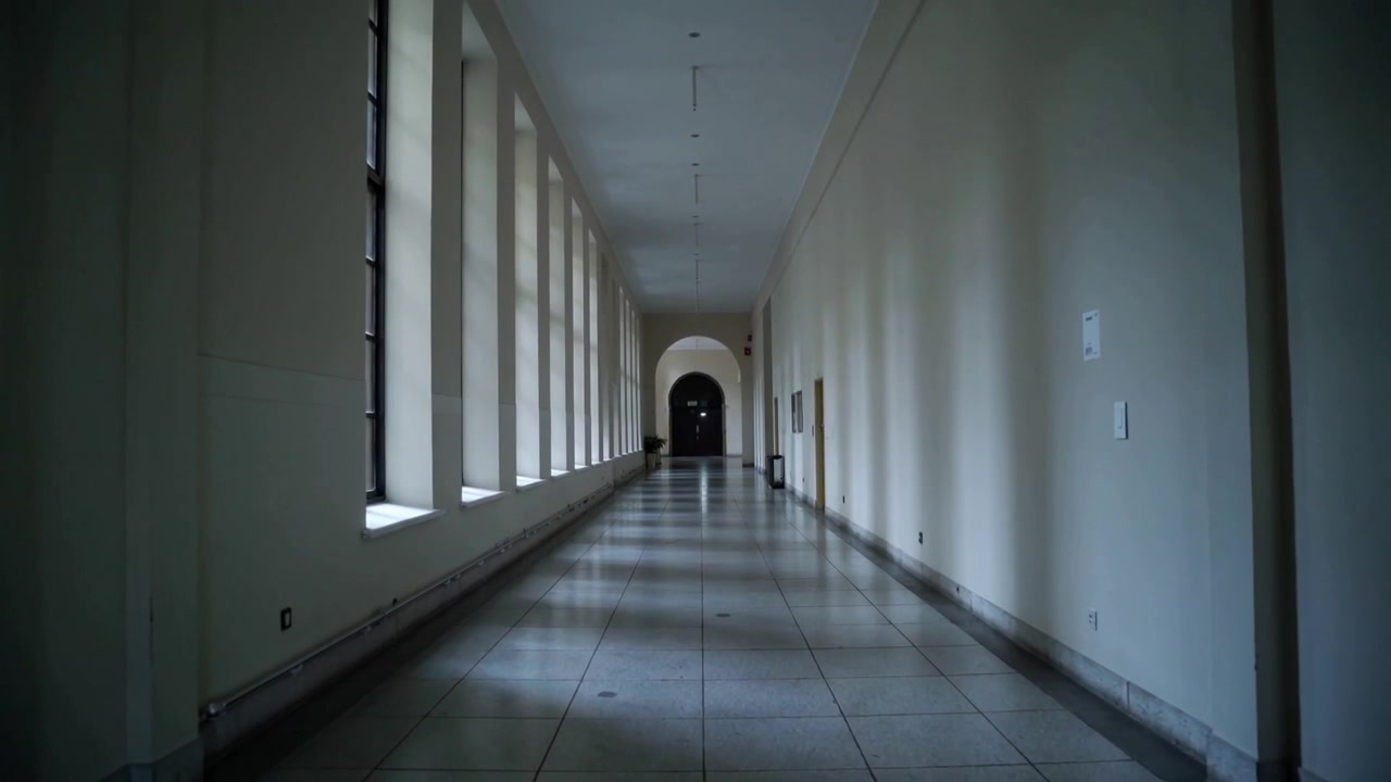 Telecamera in movimento che si sposta lungo la galleria rivelando alte finestre, un portale ad arco, luce cangiante sul pavimento