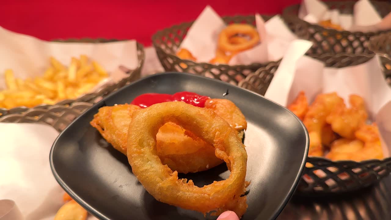 Close-up of sauces being poured on fried onion rings in a vibrant restaurant setting with fries and shrimp