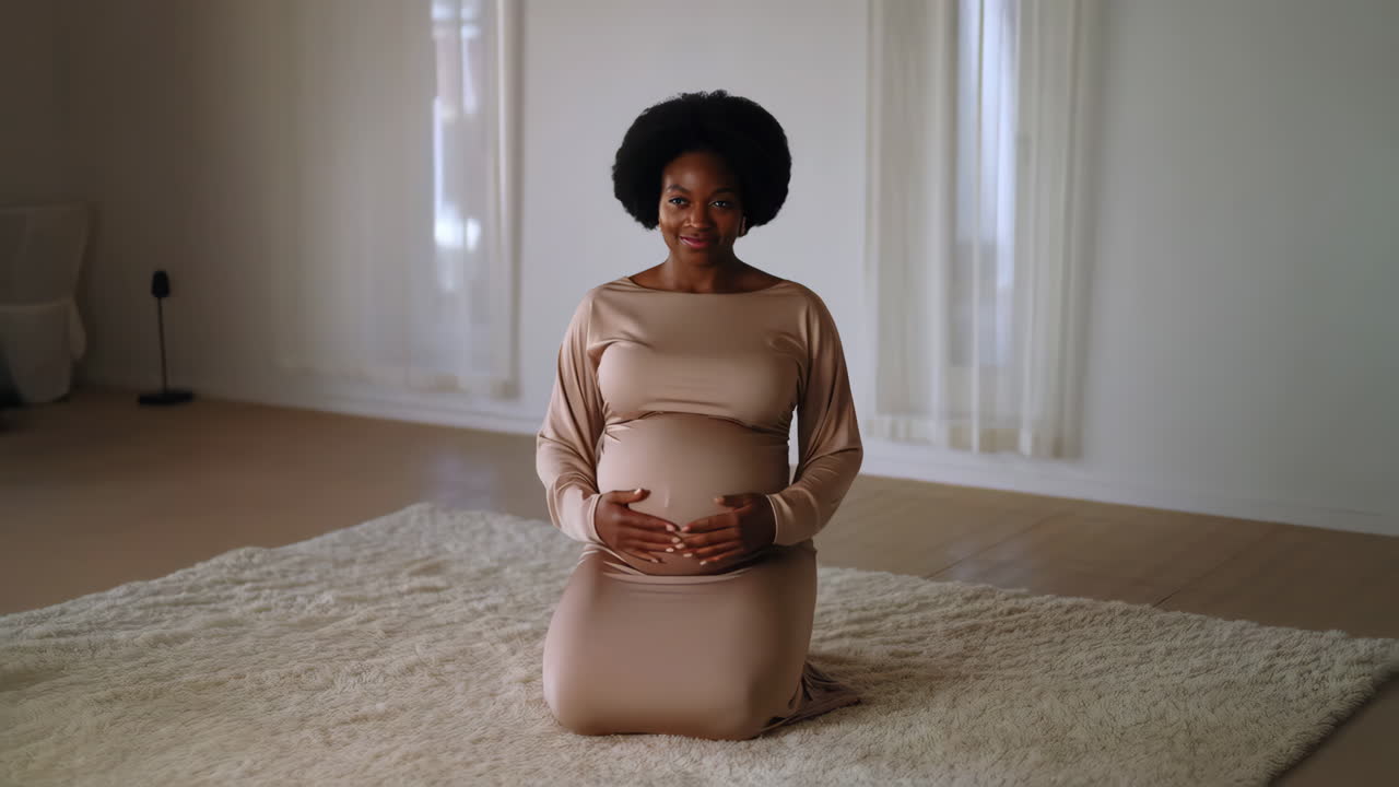 A happy pregnant woman kneeling and cradling her baby bump