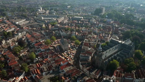 Volando-Hacia-El-Hito-Prominente-Y-La-Estructura-De-La-Iglesia-De-Sint-jan,-El-Antiguo-Ayuntamiento-Y-Los-Puestos-De-Mercado-En-El-área-Metropolitana-De-Gouda,-Países-Bajos