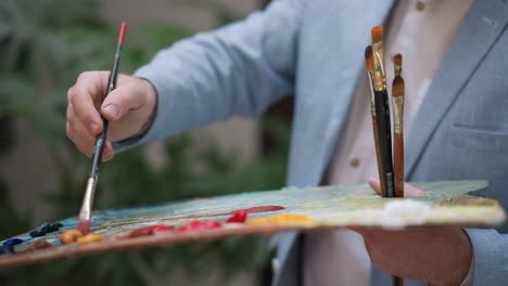 artist mixes colours on palette closeup. art teacher shows new shades making at lesson in workshop. creative painter prepares for drawing in studio