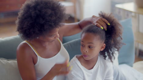 donna afroamericana che pettina i capelli della figlia e fa una coda di cavallo