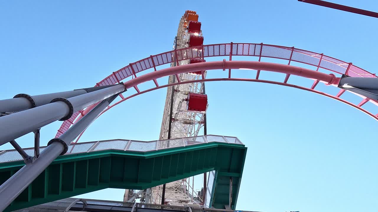 Upward View of Pink Roller Coaster Loop Framing Ferris Wheel Gondolas at Yokohama Cosmo World Against Blue Sky