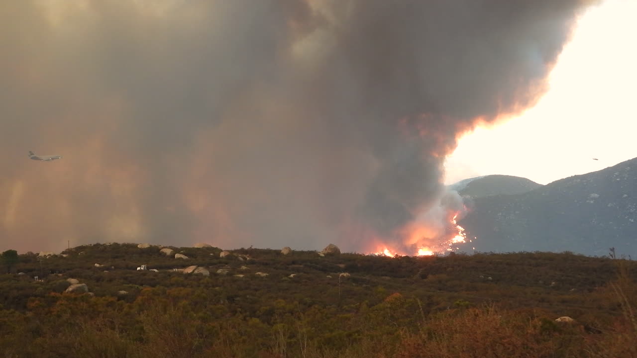 un avión vuela más allá de altas columnas blancas de humo del incendio de fairview en hemet, california