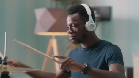 black guy practicing to play drums young african american man listening to rhythmic music in wireless headphones and playing drums during rehearsal in home studio in daytime