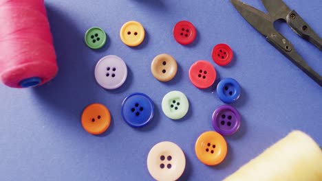 video of colourful buttons with thread snippers and reels of cotton on blue background