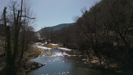 Vista-Aérea-De-Drones-Sobre-El-Paisaje-Forestal-Otoñal-Del-Río-Ribes-De-Freser-En-Los-Pirineos-Catalanes,-Fuente-De-Agua-Natural,-Reflejo-Del-Sol