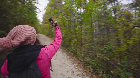 chica de senderismo con palos y mochila en un camino o sendero en el bosque de montaña. tomando fotos de sí misma con su teléfono celular. viajes y estilo de vida saludable al aire libre en la temporada de otoño. movimiento circular de la cámara..