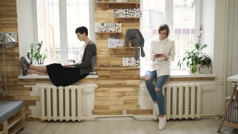 young woman using laptop sitting on window sill. woman using smart phone