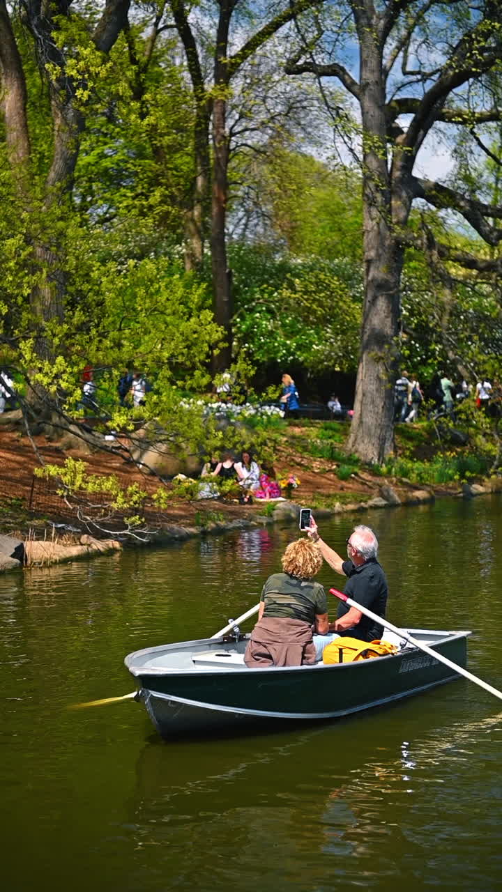 New York, USA, 12 Agustus 2025: Pasangan berperahu dayung di danau Central Park. Pasangan mendayung perahu di danau Central Park selama hari musim semi yang cerah