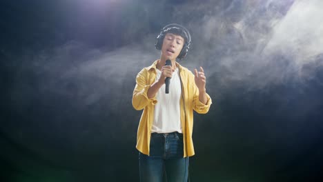 joven asiático con auriculares sosteniendo un micrófono y cantando sobre el fondo blanco de humo negro