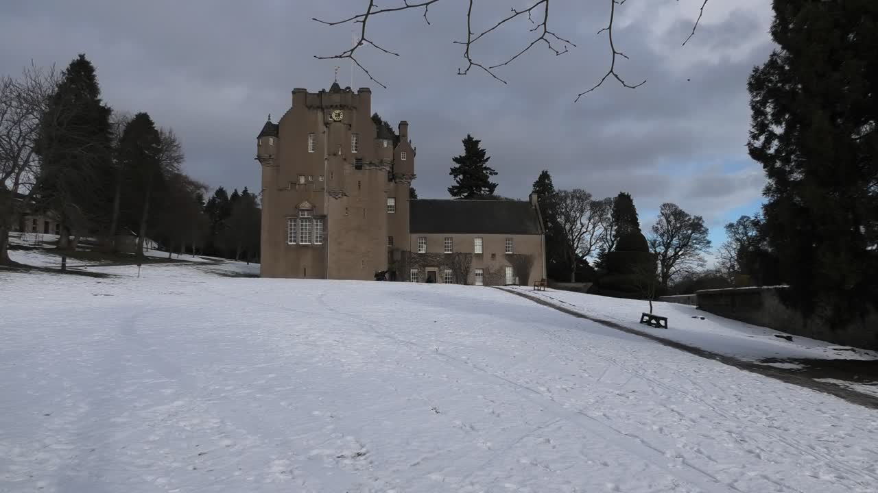 castillo de crathes en la nieve iluminada por el sol con cielo nublado