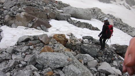 a crystal seeker mountaineer walks on rocks next to a snow plain, he has all his equipment, helmet and pickaxe, swiss alps