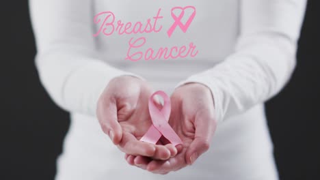 Breast-cancer-with-ribbon-forming-a-heart-icon-against-mid-section-of-woman-holding-a-pink-ribbon