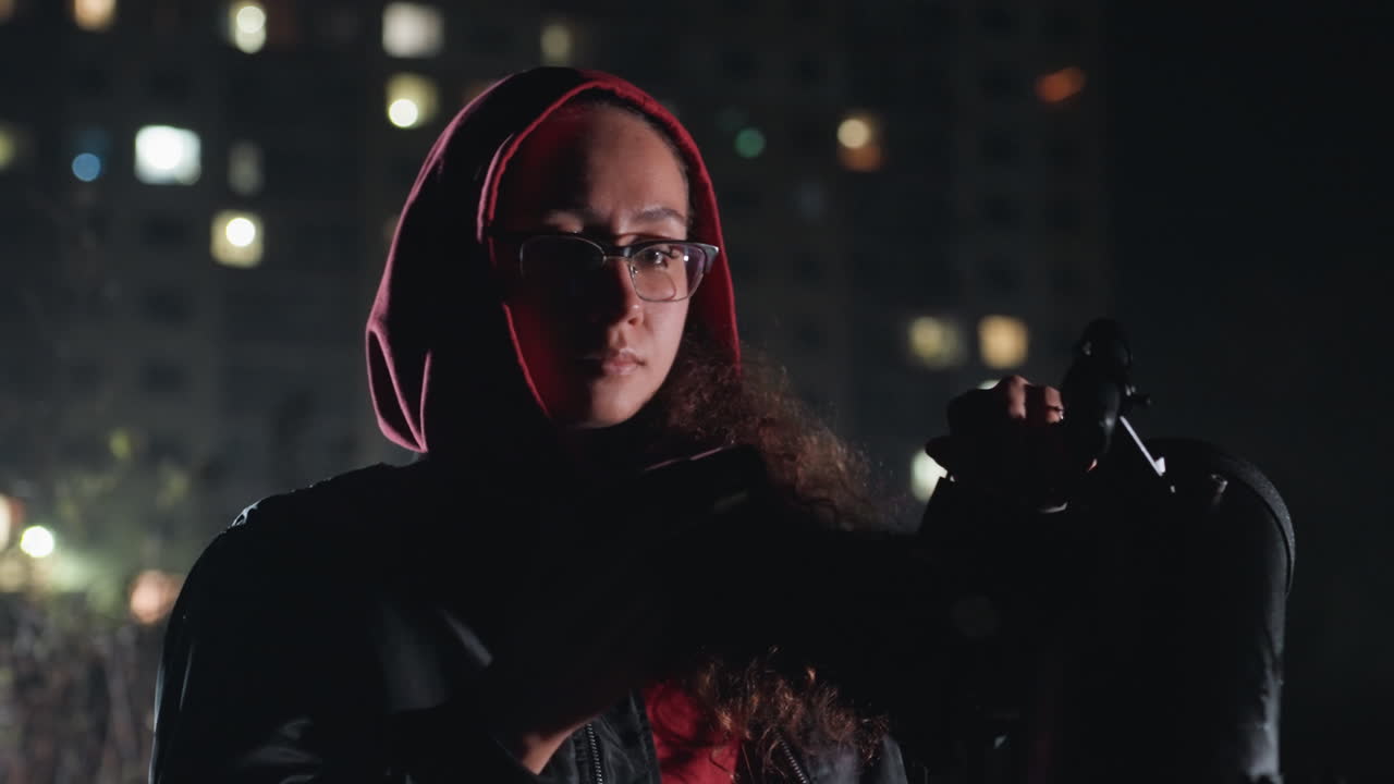 rooftop night stargazer checks telescope and binoculars under city lights, hooded woman with glasses adjusts scarf and equipment moody lowlight portrait capturing quiet scientific curiosity, amateur
