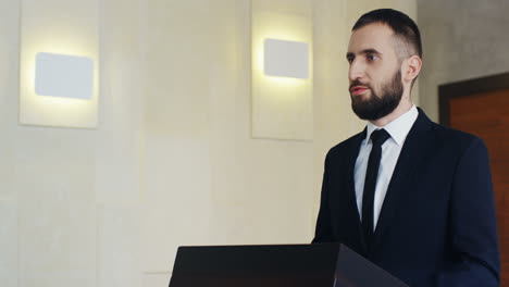 close-up view of caucasian businessman wearing formal clothes on a podium and speaking at a conference in front of many people