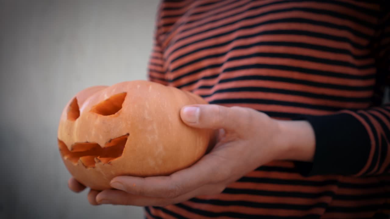 manos sosteniendo calabaza malvada con sonrisa y ojos cortados con viñeta estética y colores de cine, aspecto de halloween