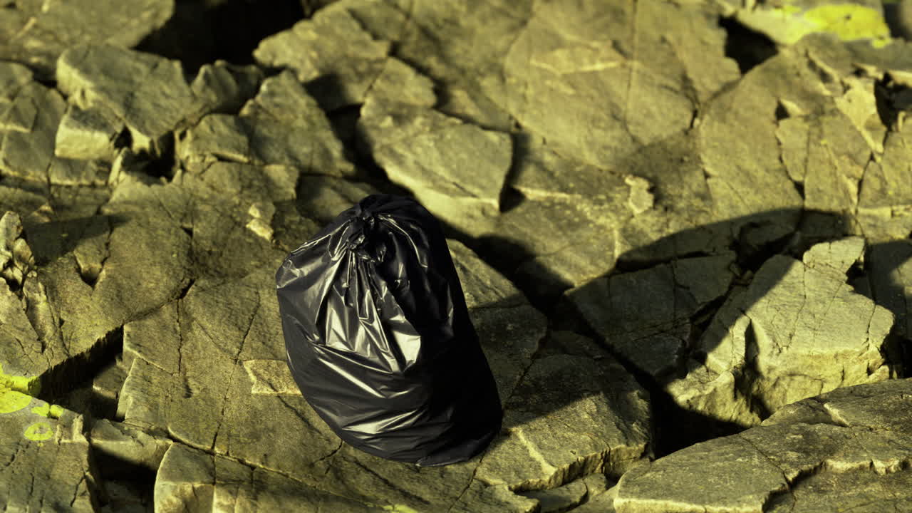 Black trash bag resting on rugged rocks with greenish tint in natural light
