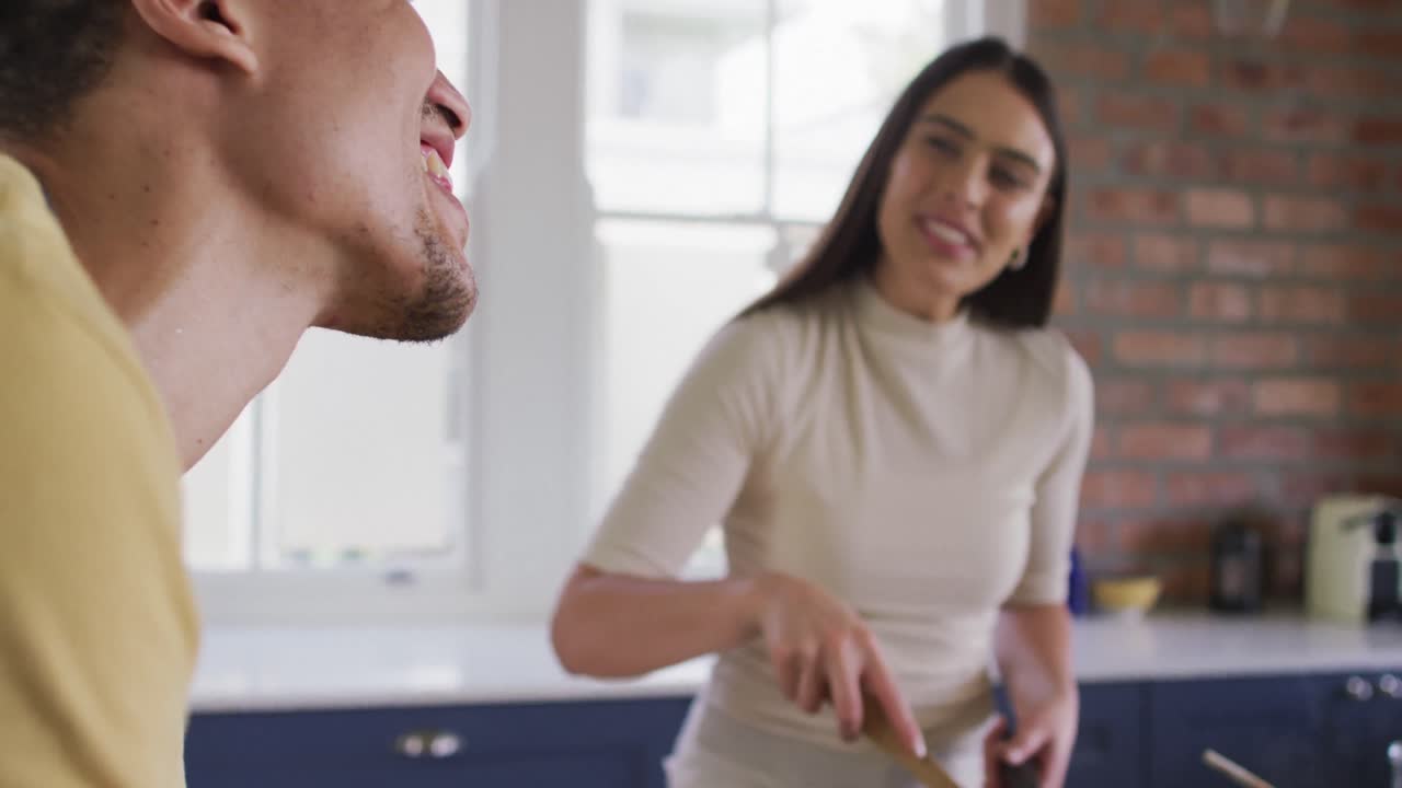 feliz pareja biracial cocinando juntos y bebiendo vino en la cocina