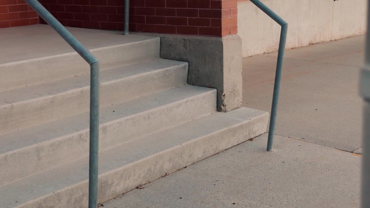 Slow right-to-left glide behind metal fence reveals concrete stairs and metal handrails.