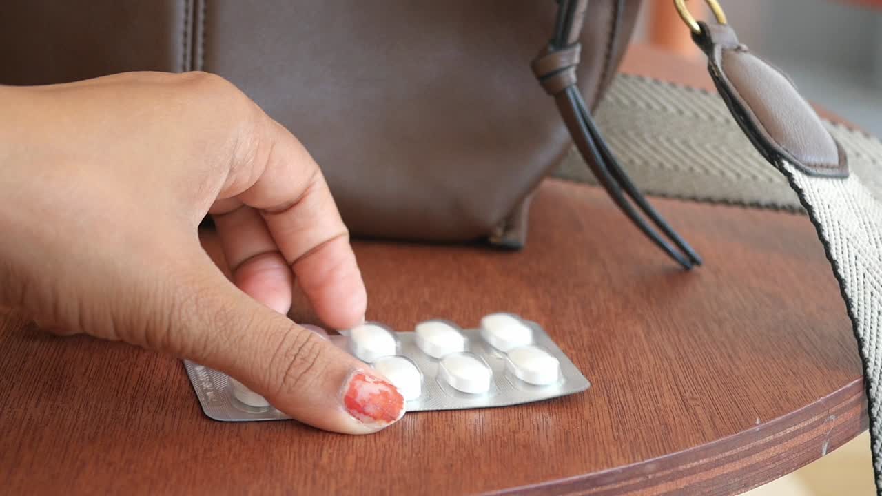 Donna che tiene un blister di pillole su un tavolo accanto a una borsa marrone