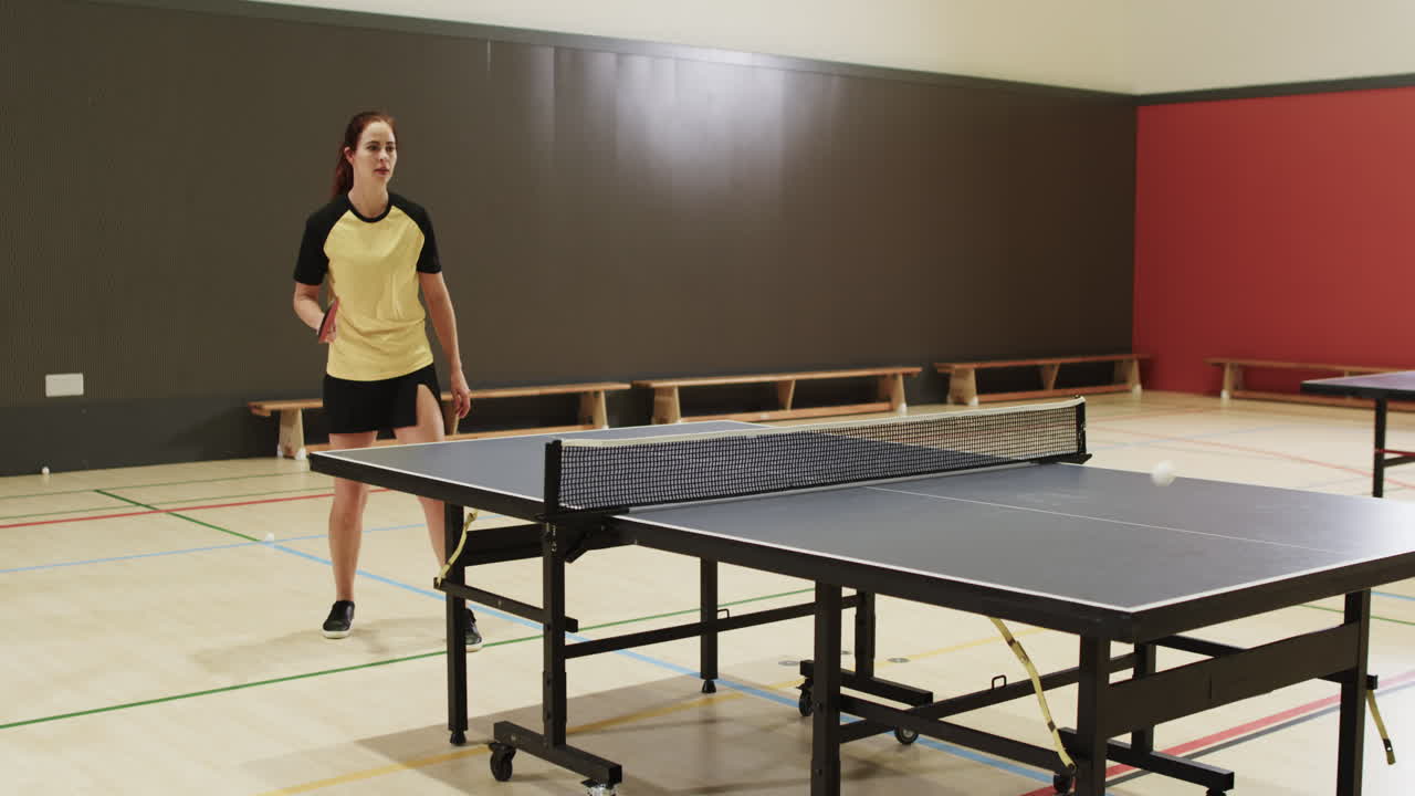 Jugando al tenis de mesa, una mujer golpea la pelota con la pala en un pabellón deportivo cubierto.
