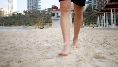 adult wearing shorts walking across white sandy beach and city background