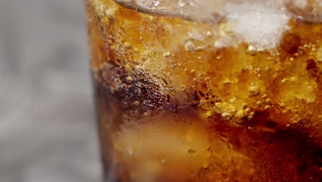 fotografía en primer plano de una bebida gaseosa marrón con hielo en un vaso burbujeante