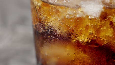 close-up shot of a brown soft drink with ice in a bubbling glass