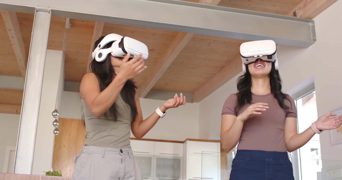 Amiche di diverse etnie che indossano visori VR si protendono e toccano in cucina, esplorando un mondo virtuale