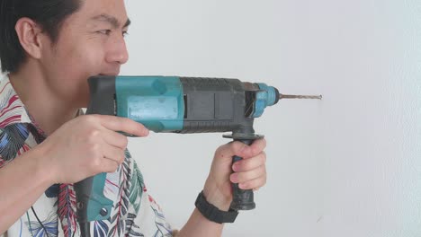 un hombre asiático usa un taladro eléctrico para taladrar la pared.