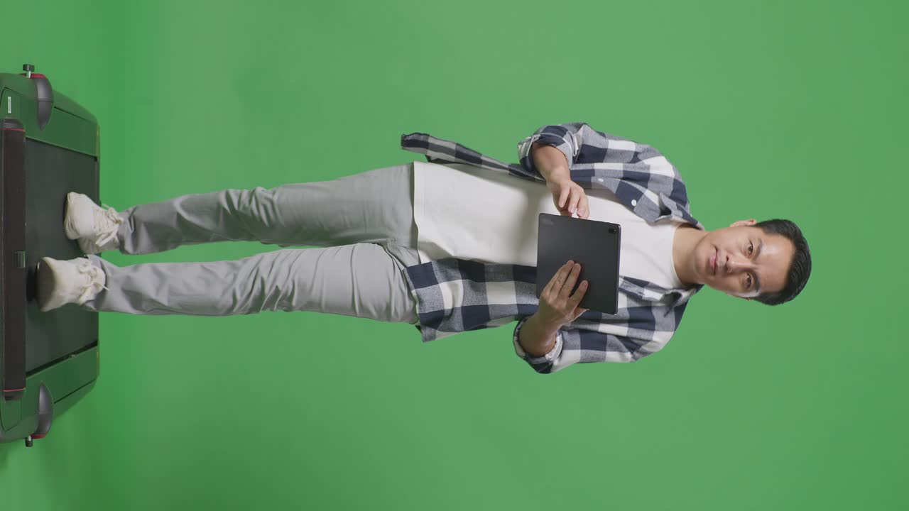 cuerpo lleno de hombre asiático usando tableta mientras camina en la pantalla verde en el estudio