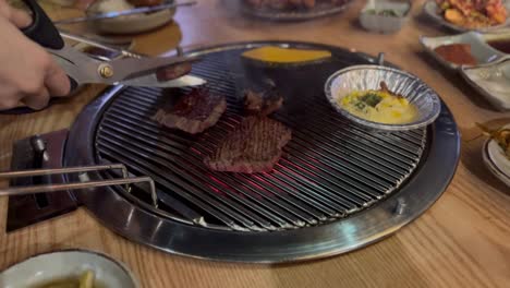 hands cut and turn smoking beef with tongs on a hot korean barbecue grill