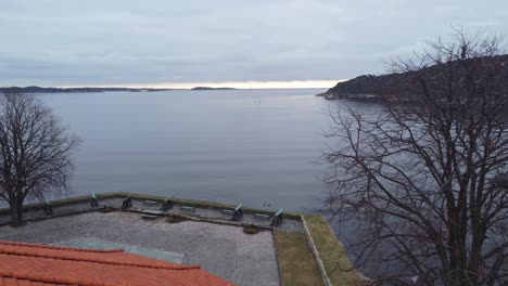 aerial flying over red roof of kristiansand fortress looking towards north sea and coastline with canons on square below - early morning aerial