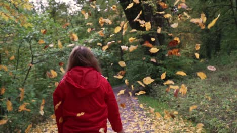 Mujer-Con-Chaqueta-Roja-Lanzando-Hojas-De-Otoño-Al-Aire