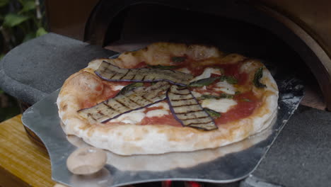 el chef pone berenjenas a la parrilla encima de la masa de pizza napolitana y la gira en la bandeja