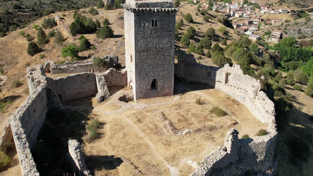 Vista in volo all'indietro di una torre medievale in un castello a Ucero, Soria, circondato da mura, sulla cima di una collina