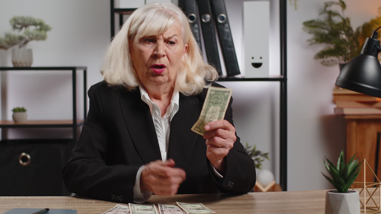 Elderly businesswoman in suit counting cash banknotes insufficient amount of money at home office