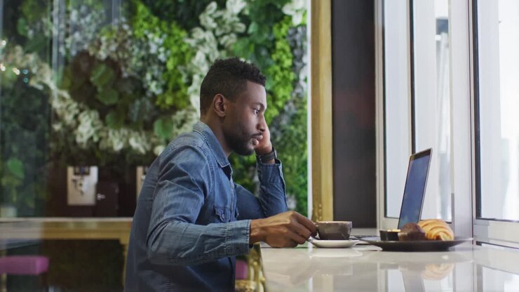 African american businessman using laptop drinking coffee in cafe