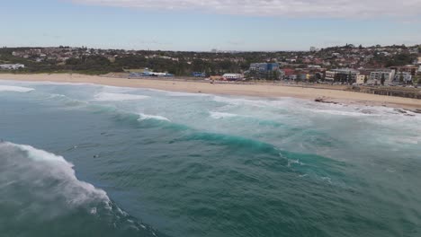 aerial view of maroubra beach with strong waves, surfers, swimmers, sandy shoreline, and distant cityscape on a cloudy day – coastal australia