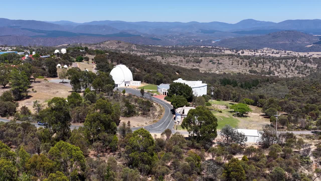Wide aerial drone shot of white observatory domes nestled in the Australian bush landscape