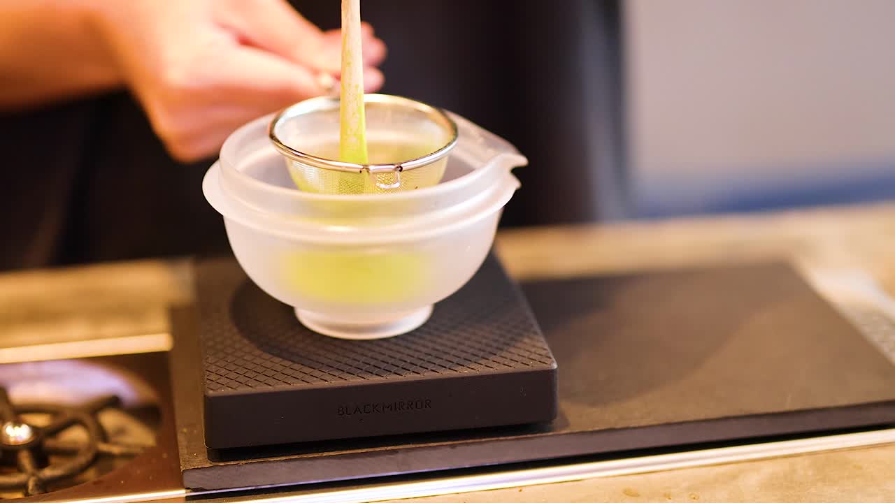 Hands whisk matcha in a bowl on a scale, highlighting traditional tea-making techniques with precise movements and vibrant green color