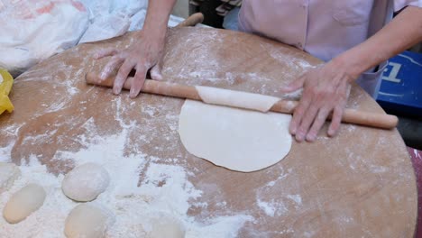 woman rolling out dough with a wooden rolling pin on a table