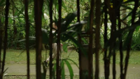 Beautiful-young-woman-walking-and-exploring-the-jungle-on-a-paved-stone-path-shot-through-the-bamboo-tree-in-a-shade-with-backpack-and-fanny-pack-walking-on-steps-Ubud-Bali-Indonesia