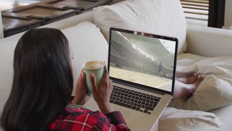 compuesto de una mujer sentada en casa sosteniendo café viendo un evento de salto de longitud de atletismo en una computadora portátil