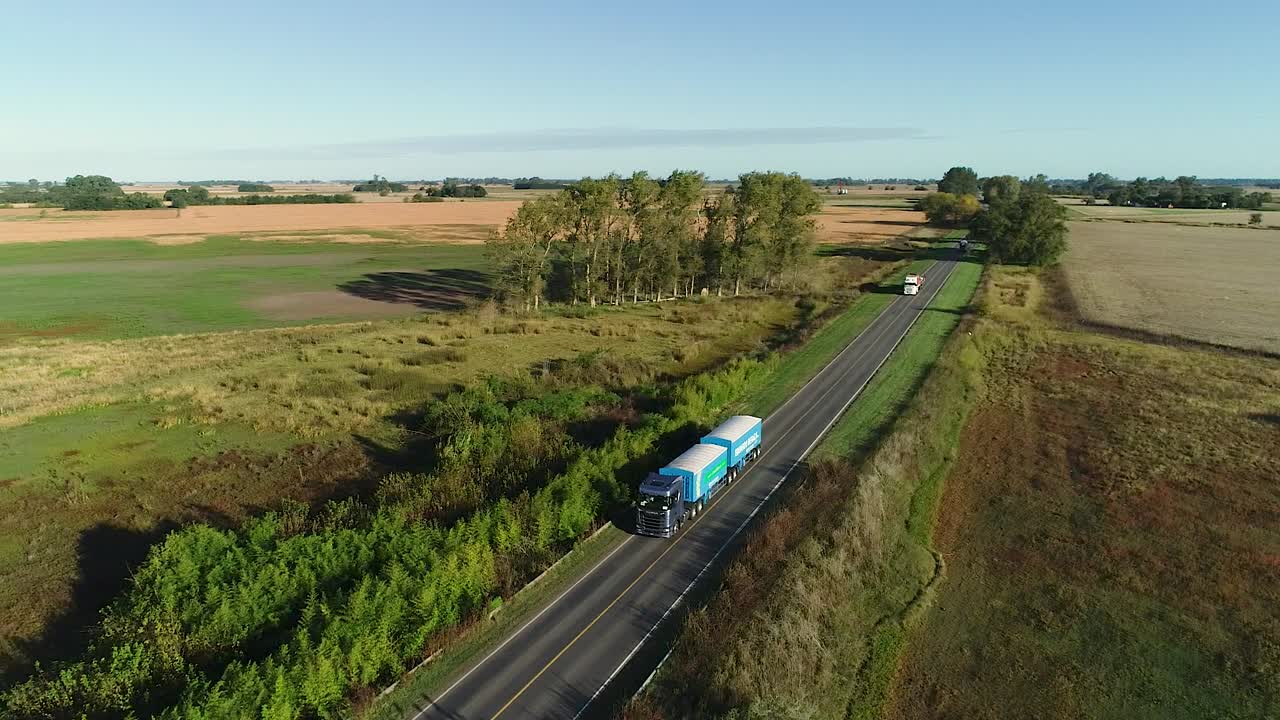 fotografía aérea de camiones conduciendo a lo largo de una carretera rural en un día soleado, arrojando largas sombras
