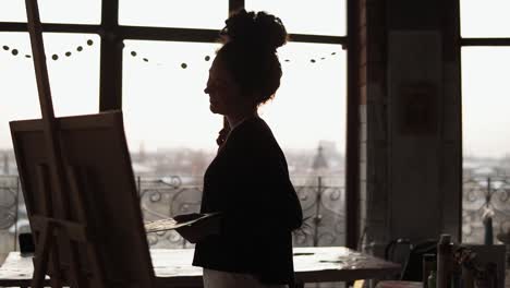 Young-Sweet-Female-Artist-Dancing-While-Drawing-Her-Picture-With-Paint-Palette-In-Her-Hands,-In-The-Loft-Styled-Art-Studio