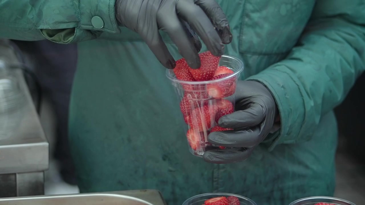Person in Green Jacket Packing Fresh Strawberries into Plastic Cup