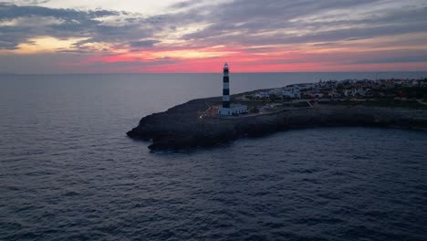 lighthouse glowing, aerial drone fly sunset sky in menorca landscape over cap d’artrutx, mediterranean skyline